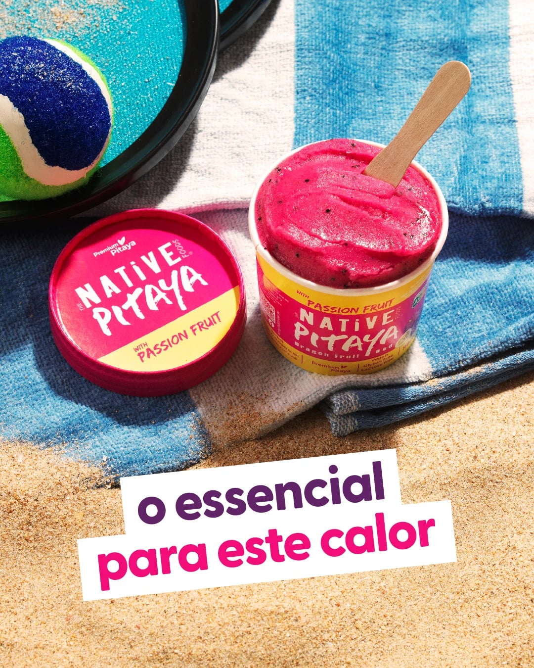 Copo de gelado rosa "Native Pitaya with Passion Fruit" sobre toalha de praia na areia com "o essencial para este calor"