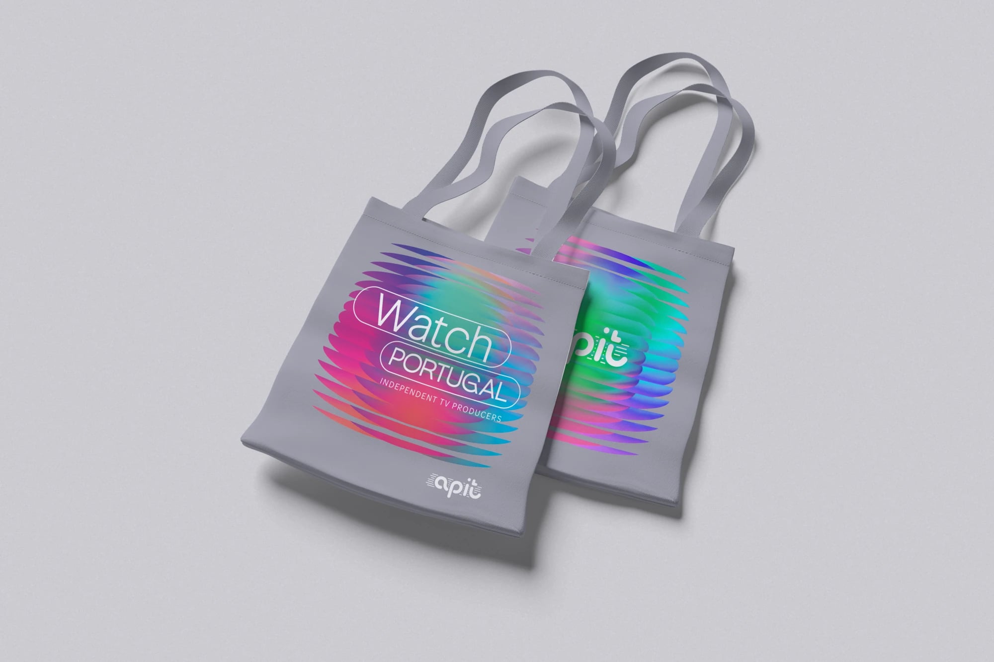Duas totebags cinzentas com gradiente colorido e os textos "Watch Portugal", "Independent TV Producers" e "apit"